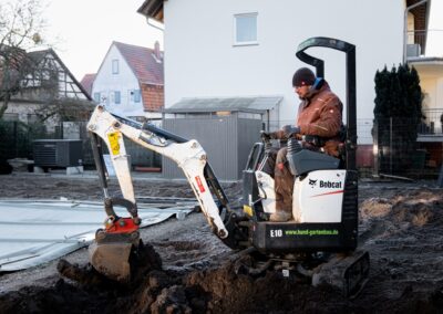Mitarbeiter von Hund Garten- und Landschaftsbau führt Baggerarbeiten für die Bodenvorbereitung auf einer Baustelle durch.