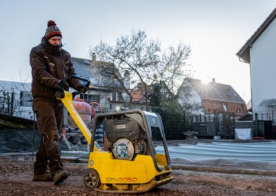 Ein Mitarbeiter von Hund Garten- und Landschaftsbau nutzt eine Rüttelplatte zur Verdichtung eines vorbereiteten Unterbaus.